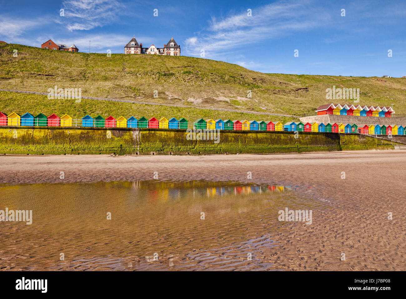 Beach huts lining the promenade and reflecting in a pool at North Beach, Whitby, North Yorkshire, England, UK, on a bright sunny spring morning. Stock Photo