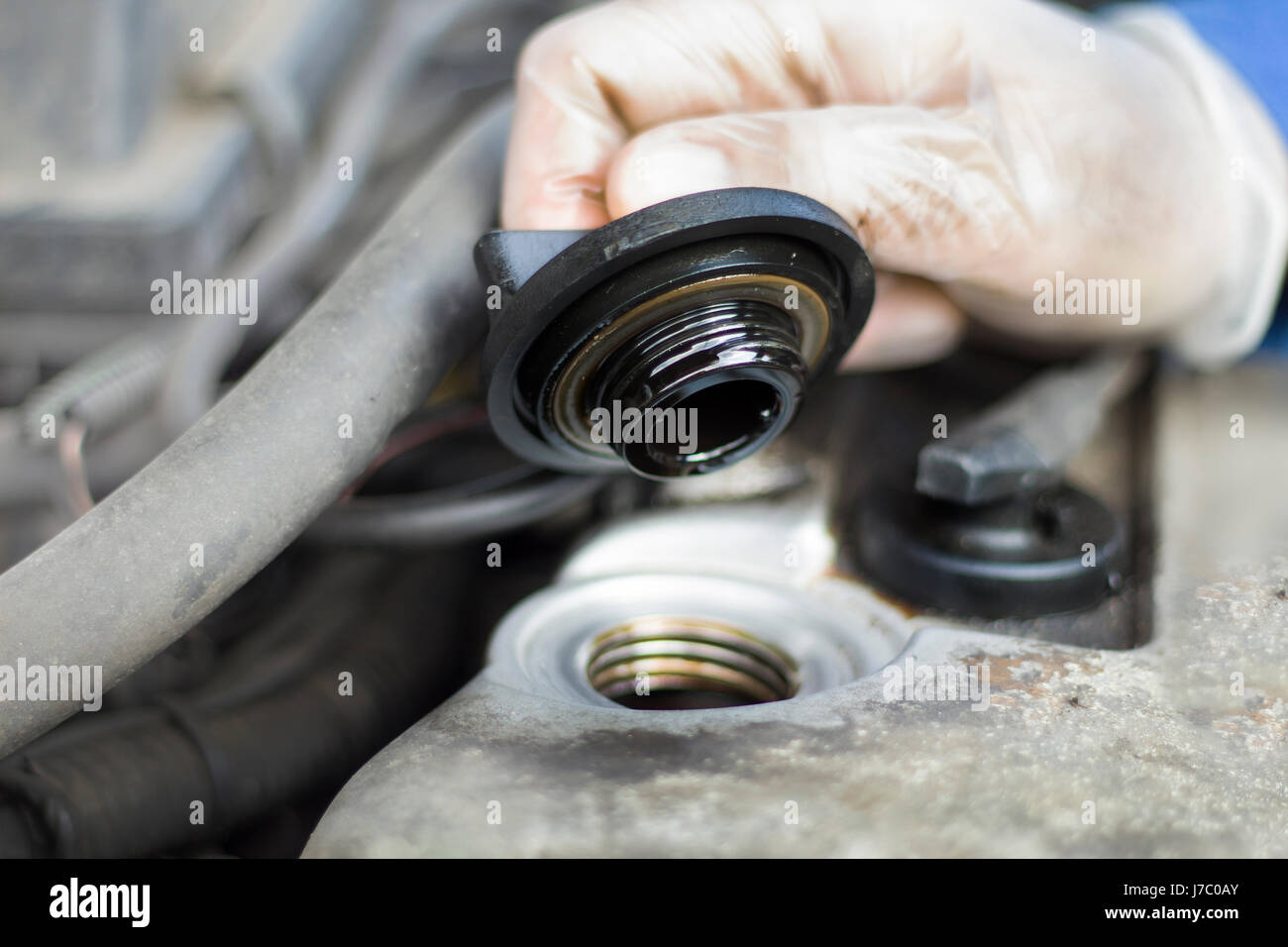 The hands of the car mechanic unscrew the cap of the oil filler. The