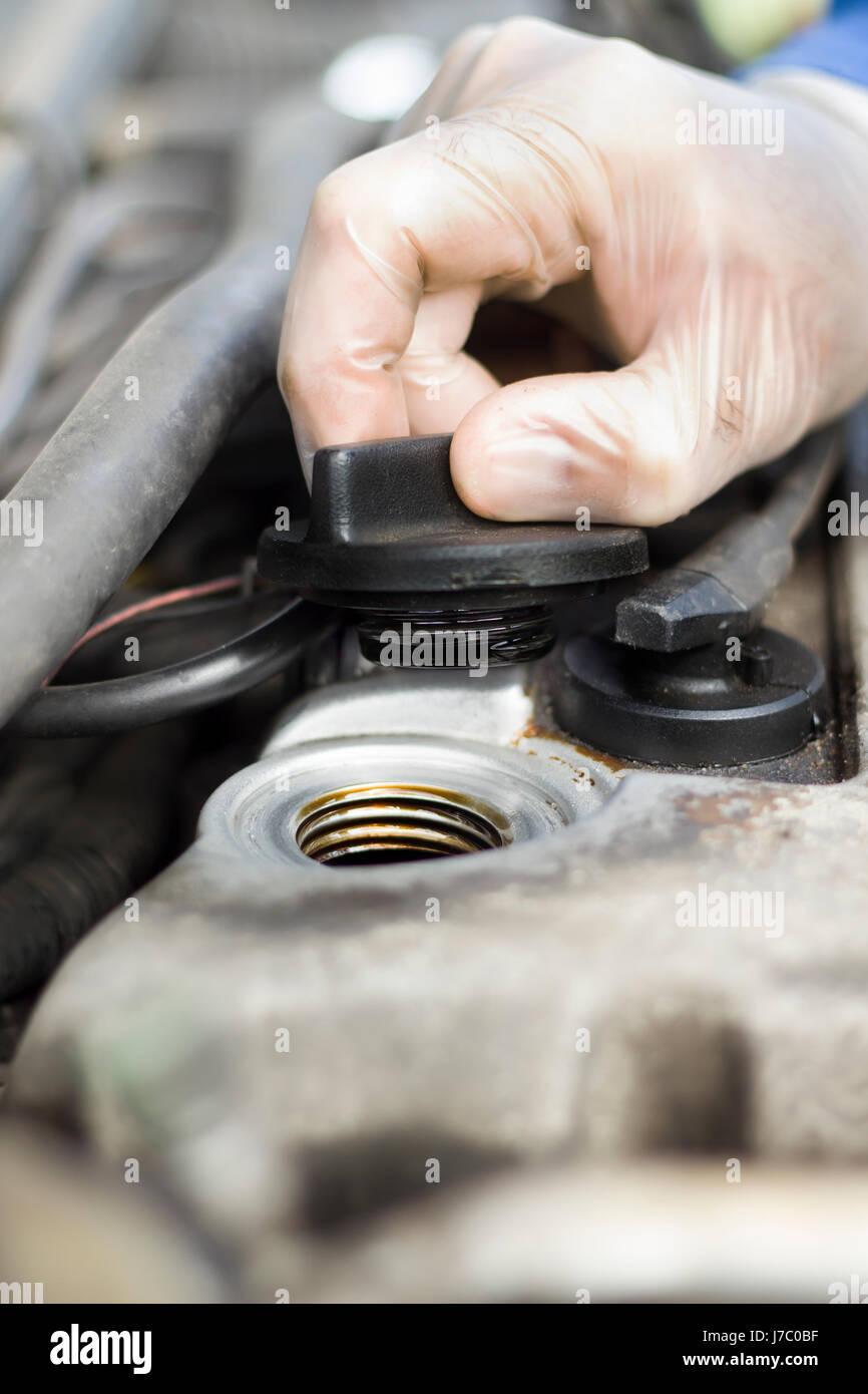 The hands of the car mechanic unscrew the cap of the oil filler. The