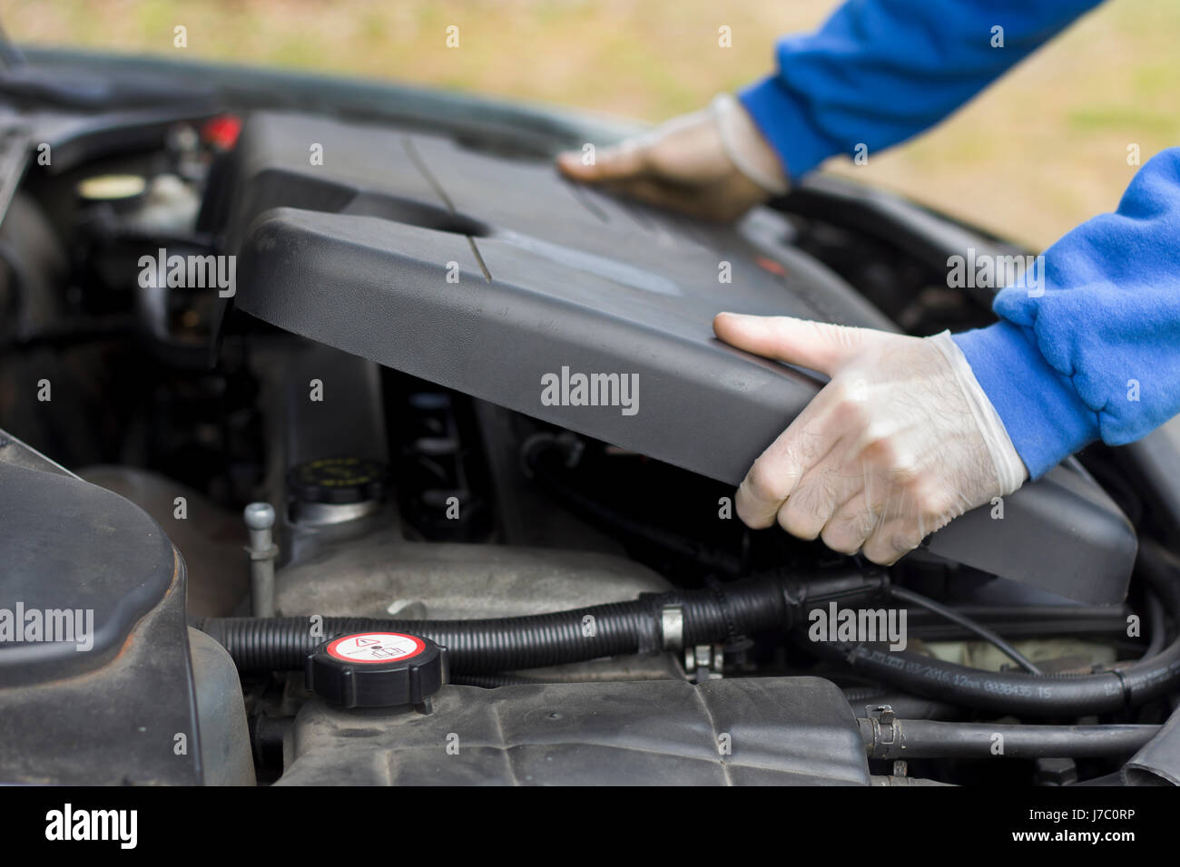 The mechanic in the removes the plastic engine cover from the