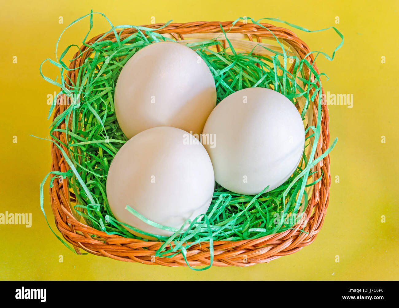Light green duck eggs, brown basket with grass, yellow background. Stock Photo