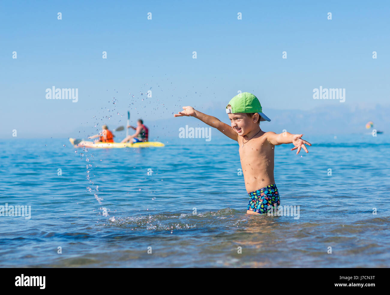 Smiling little baby boy in green baseball cap playing and splashing in the sea, ocean. Positive human emotions, feelings, joy. Grandmother and grandfa Stock Photo