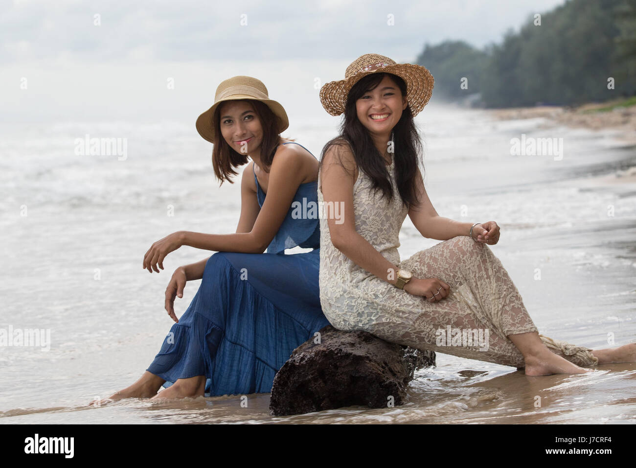 portrait of young beautiful asian tan skin  woman wearing fashion straw hat sitting on wood lock at sea beach with relaxing emotion Stock Photo