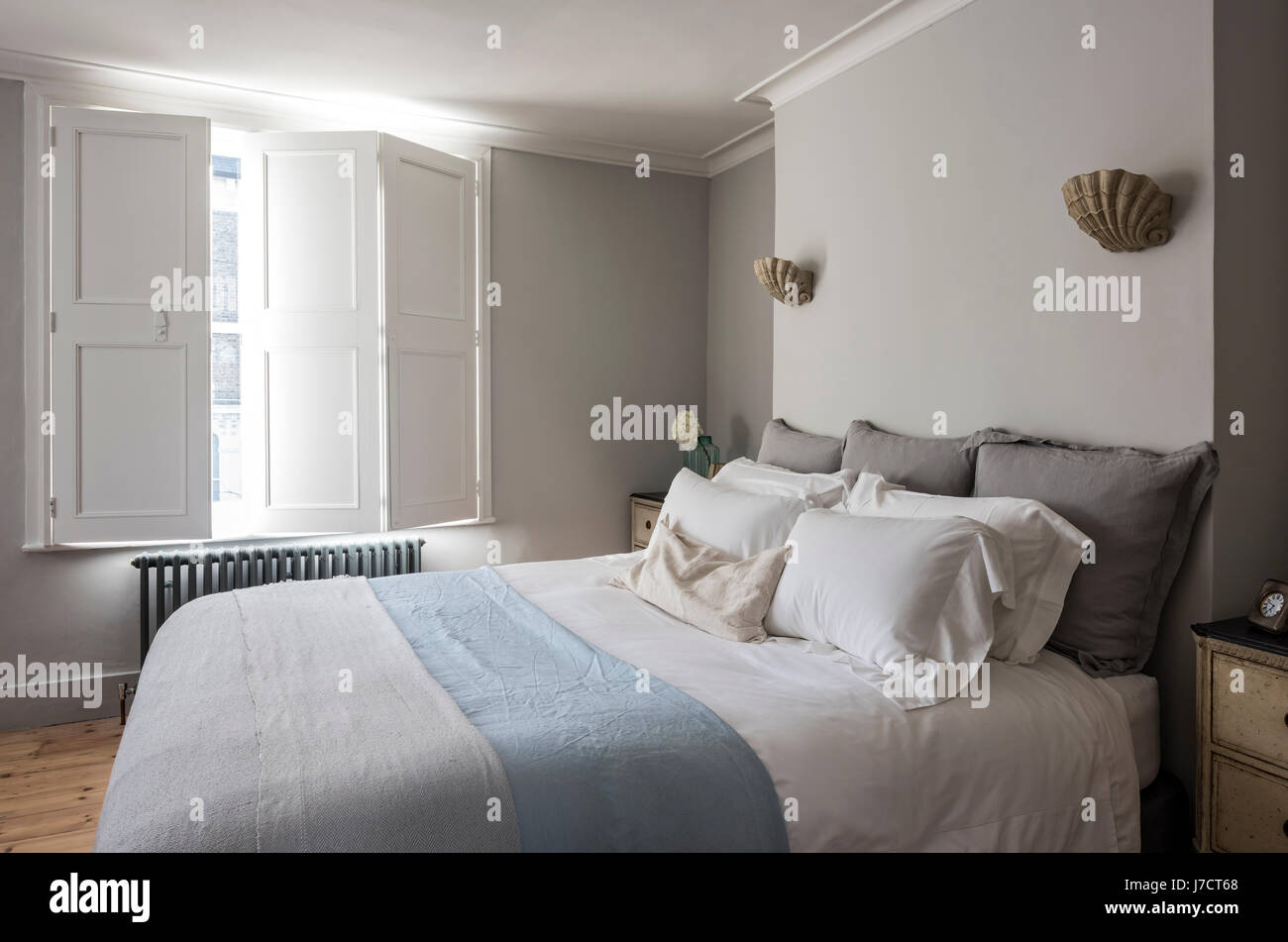 Elegant bedroom with window shutters and scallop wall sconce lights from Cox London Lighting. Stock Photo