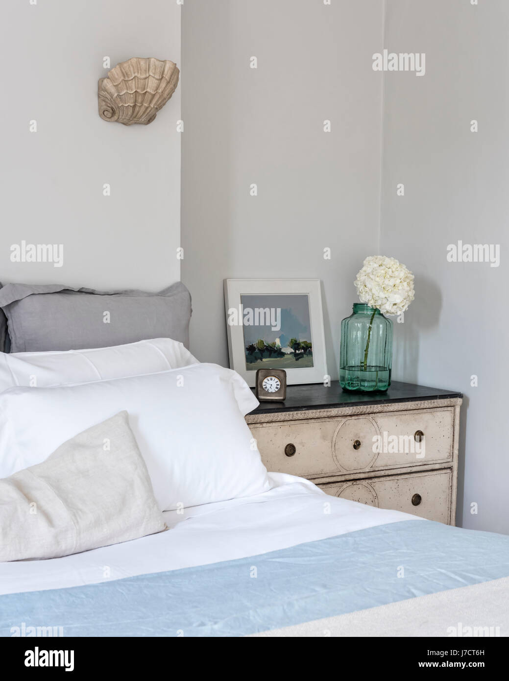 Elegant bedroom with window shutters and scallop wall sconce lights from Cox London Lighting. The bed is flanked by a pair of Gustavian painted Swedis Stock Photo