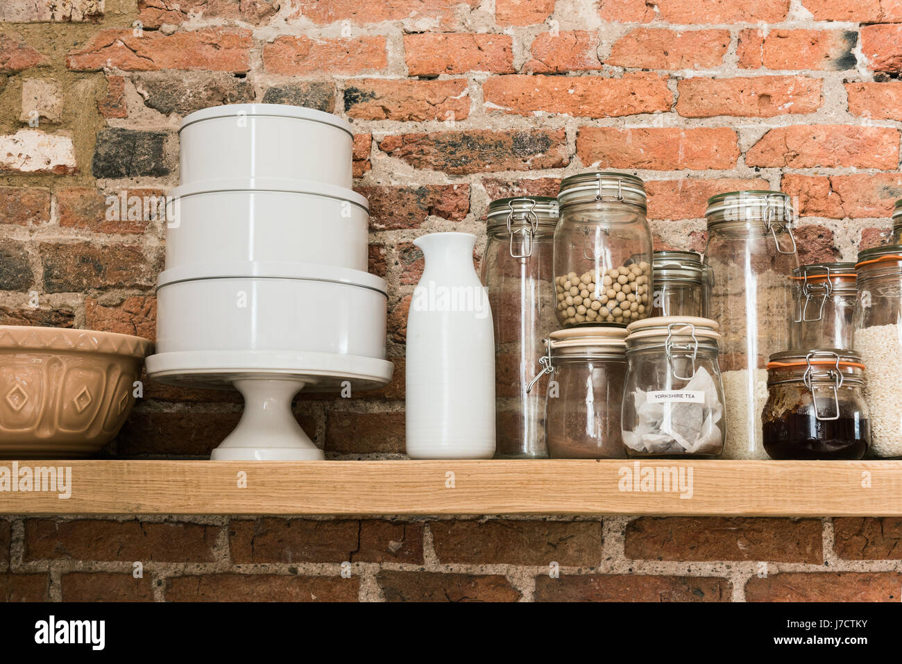 Kilner jars and cake tins on shelf against exposed brick wall Stock Photo