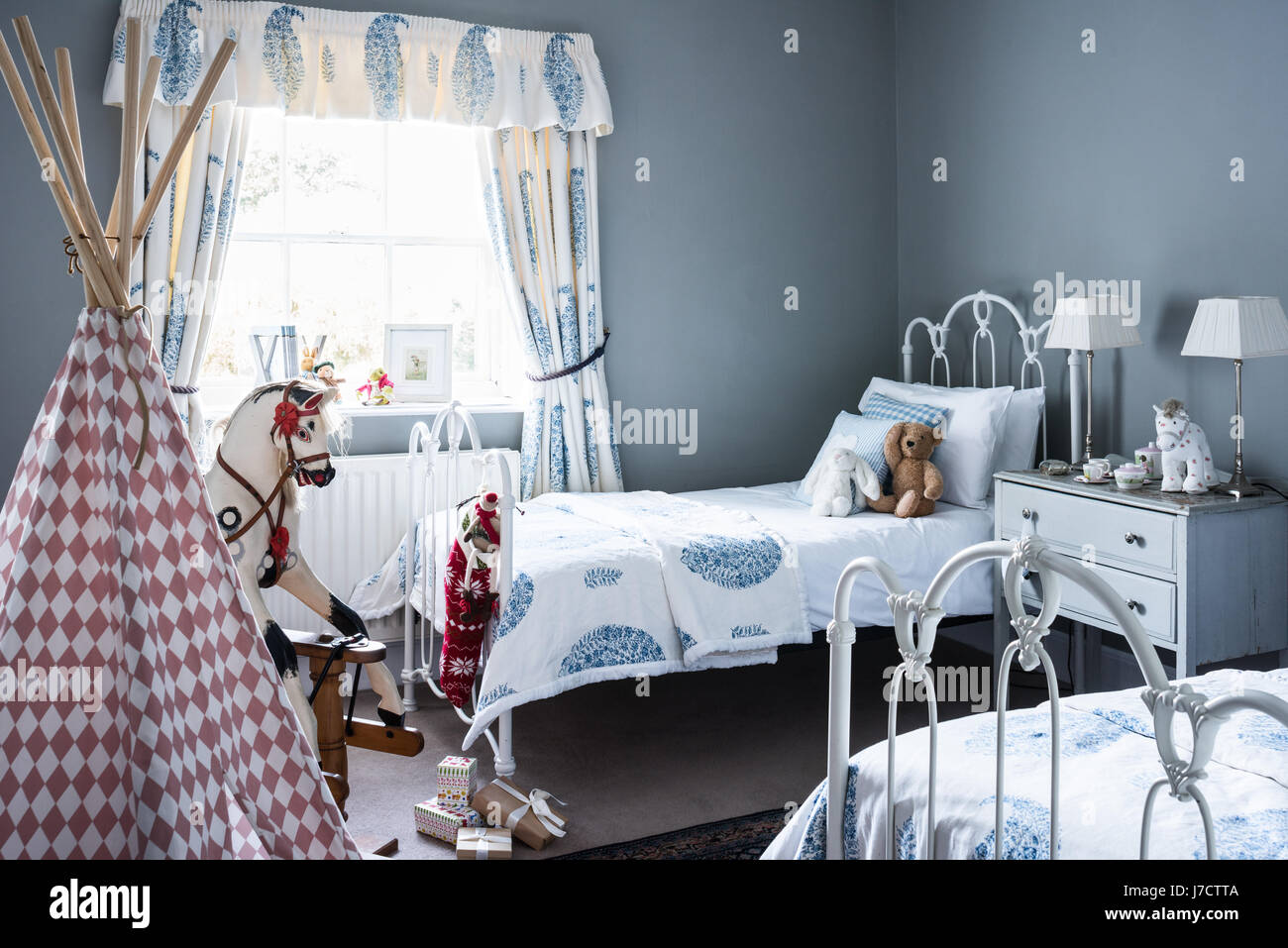 Childs bedroom with twin iron beds, old fashioned rocking horse and curtains from House of Curtains. The walls are painted in Parma Gray by Farrow & B Stock Photo