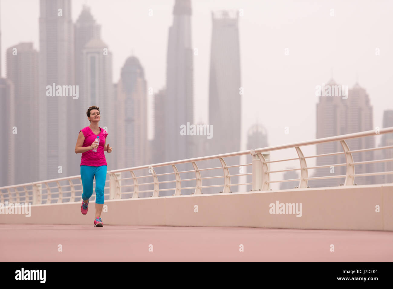 very active young beautiful woman busy running on the promenade along ...