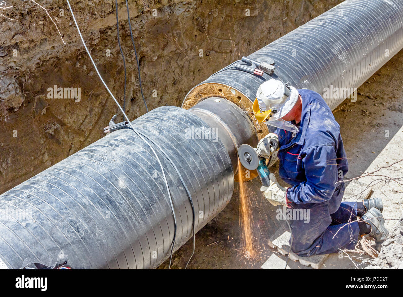 Worker is cleaning welding seam on pipeline with a grinding machine