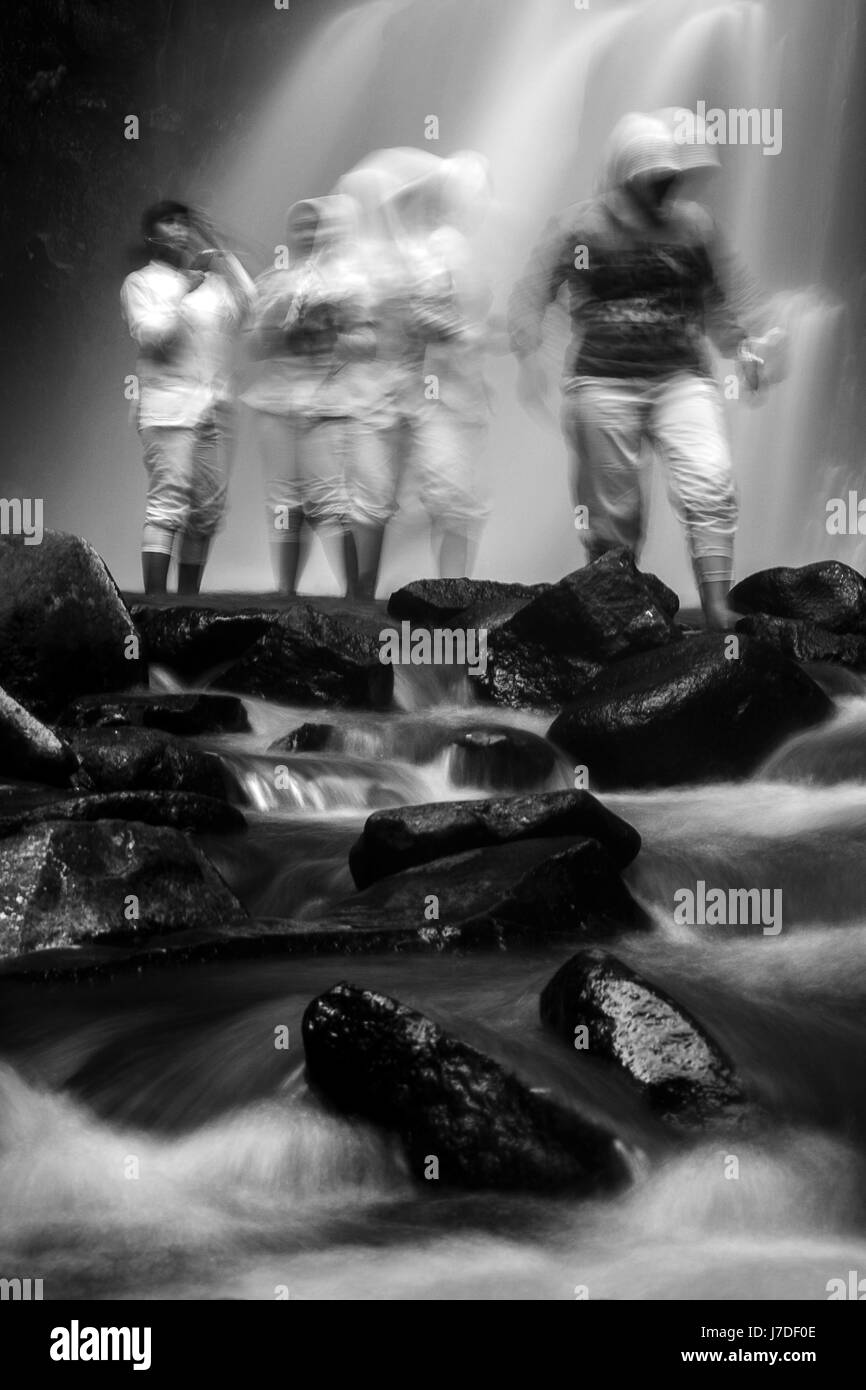 Abstract  black and white fine art photo with Muslim girls ghosted at a silky smooth waterfall in Indonesia.Created using a long exposure technique Stock Photo