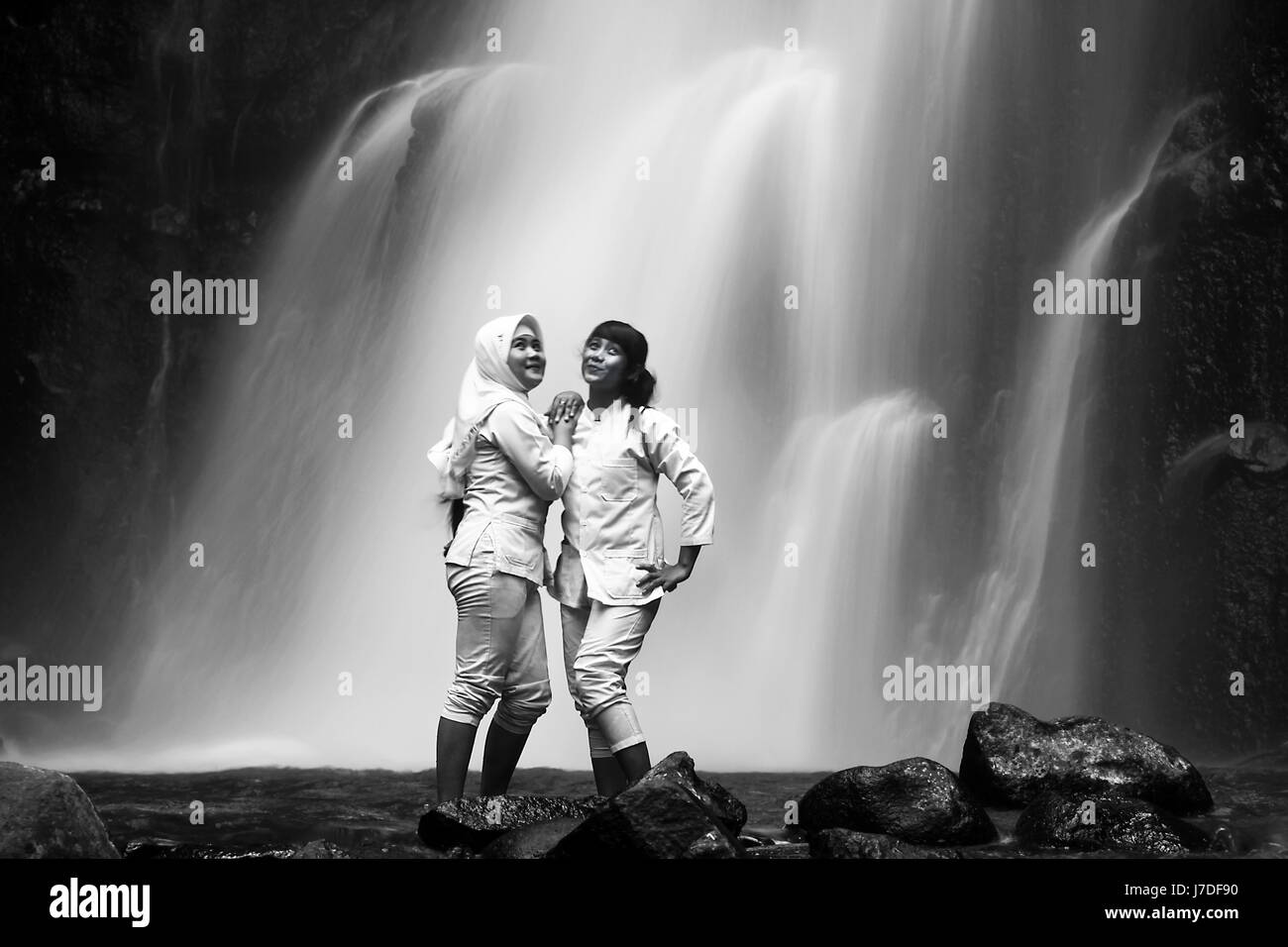 Girls posing at surreal waterfall for black and white portrait photo with ethereal silky smooth waterfall in the background. Dramatic long exposure Stock Photo
