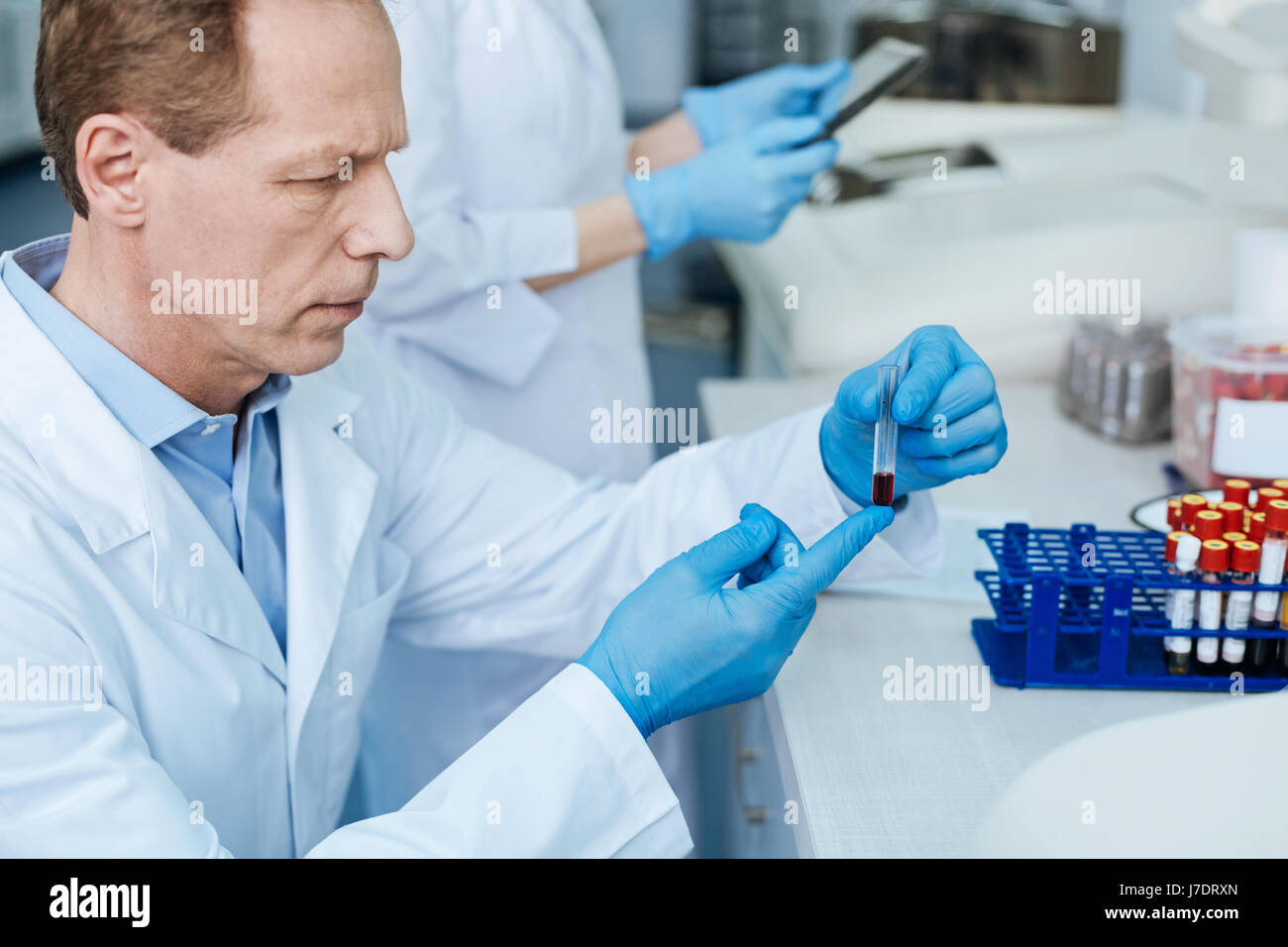 Portrait of serious scientist while looking attentively at test tube Stock Photo