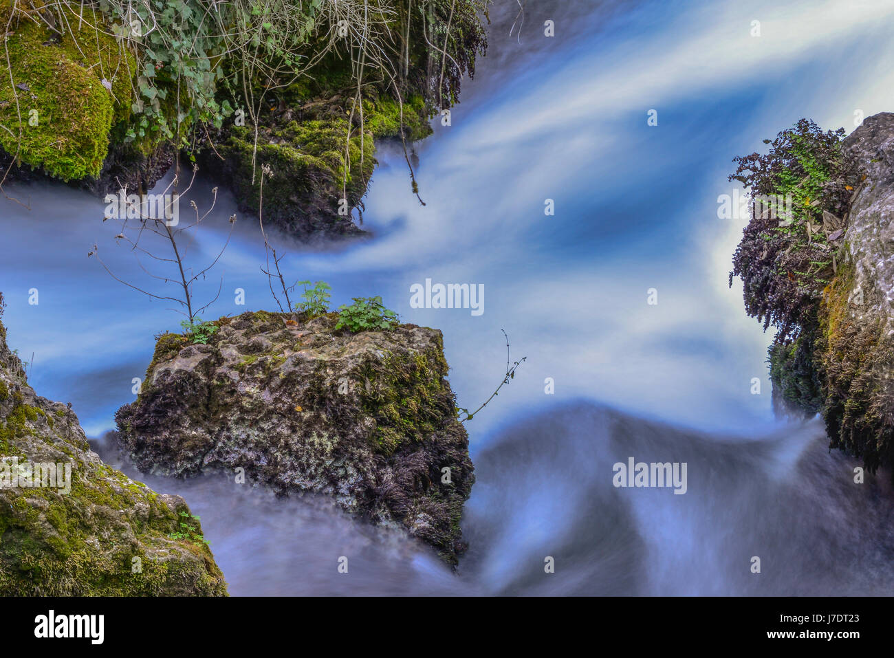 Time exposure of flowing water passing over grass covered rocks. Stock Photo