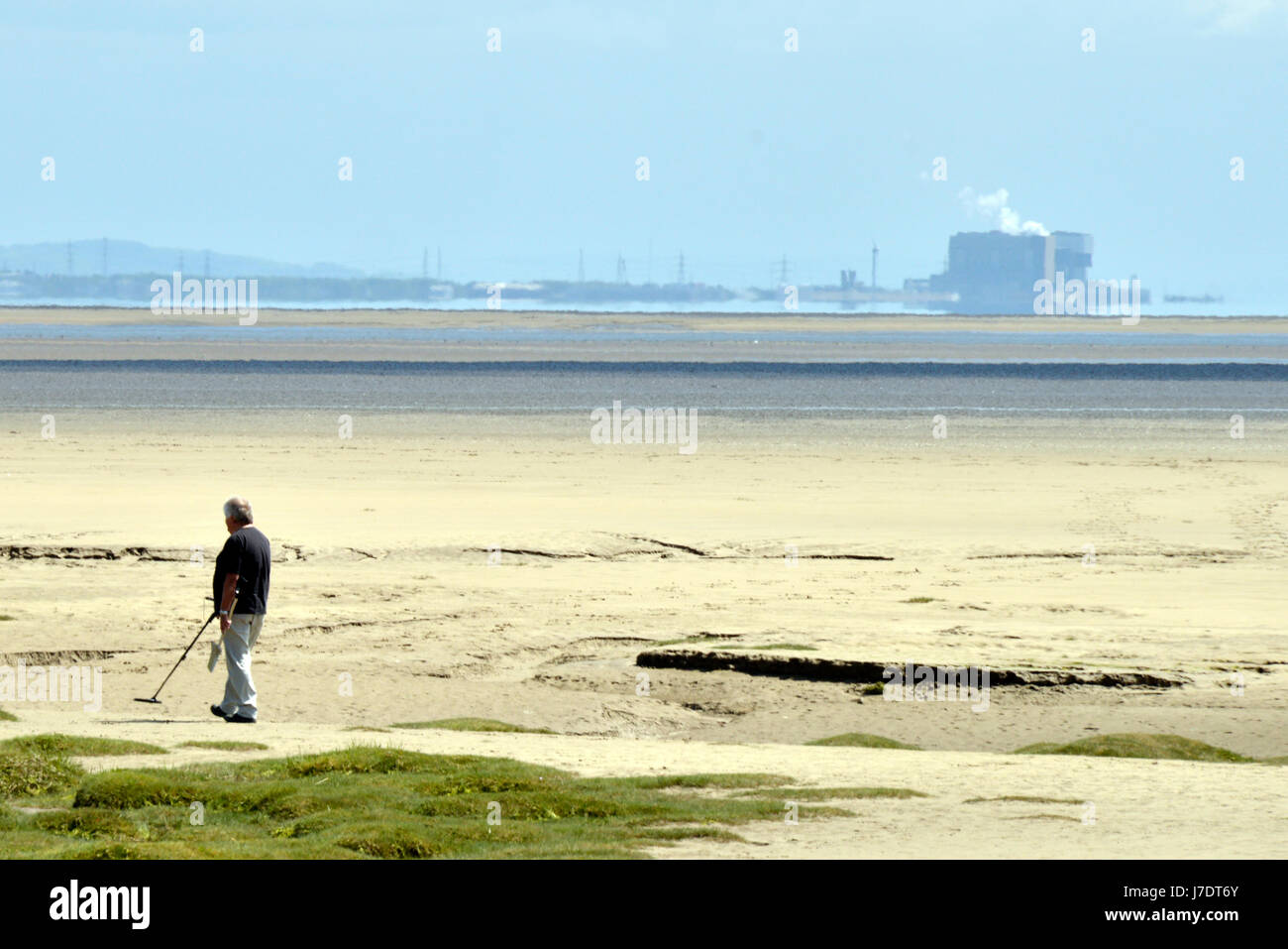 A lone man metal detecting on a desolate beach with a power station in the misty background. Taken at Barrow-in-Furness, looking towards Lancaster, UK. Stock Photo