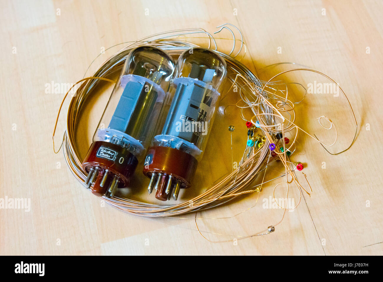 An assortment of used electric guitar strings and a pair of EL34B valves from a valve amplifier on a wooden surface. Stock Photo