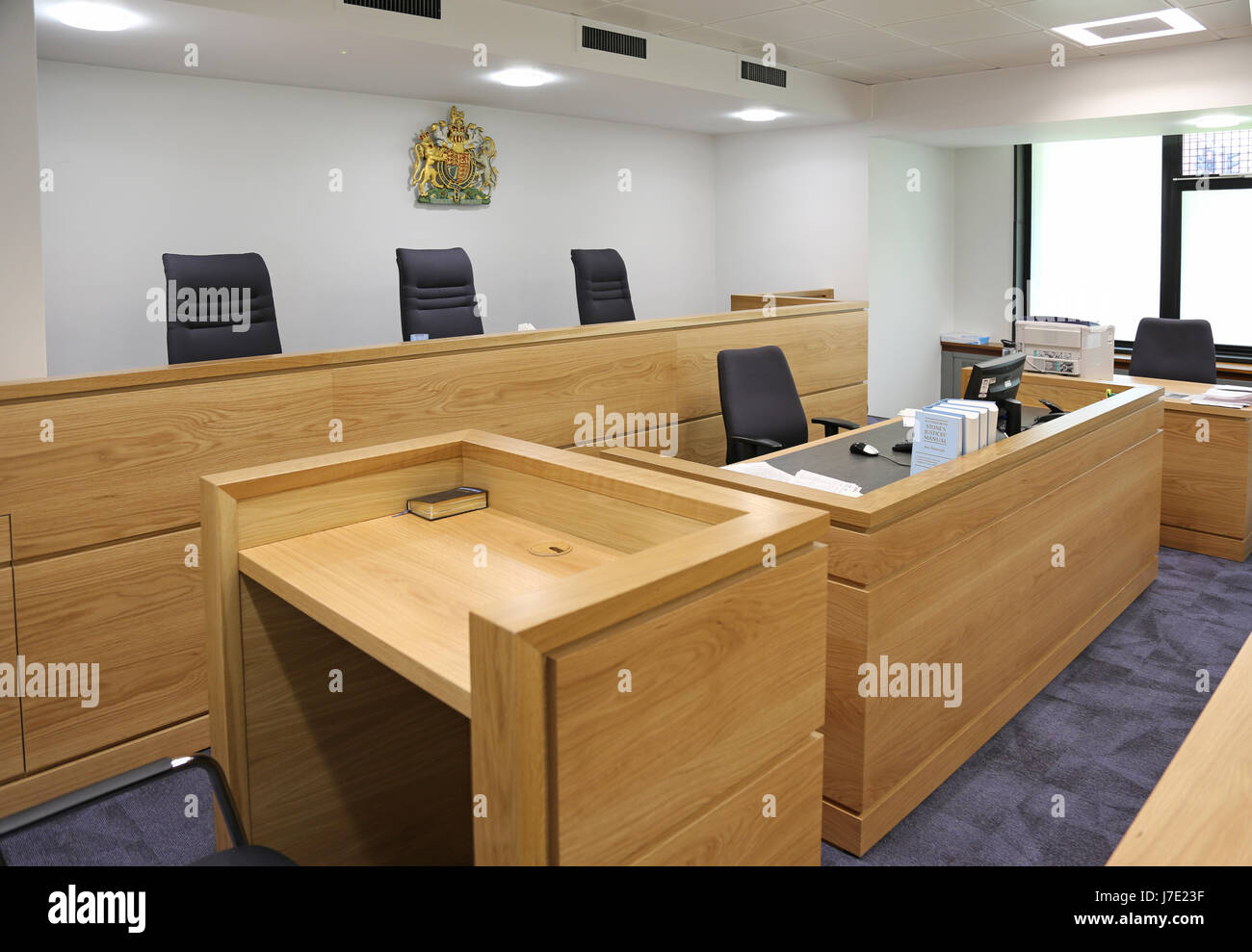 Interior of a modern, English courtroom. Shows judges/magistrates bench and witness box (with Bible) in the foreground Stock Photo
