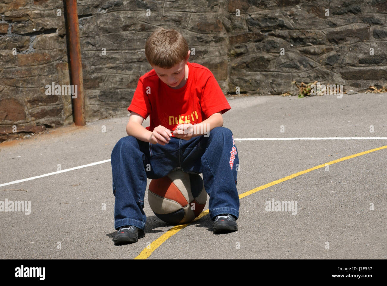 The Tai Centre, Penygraig, Wales, with a lonely boy sitting on his football in the playground. Stock Photo