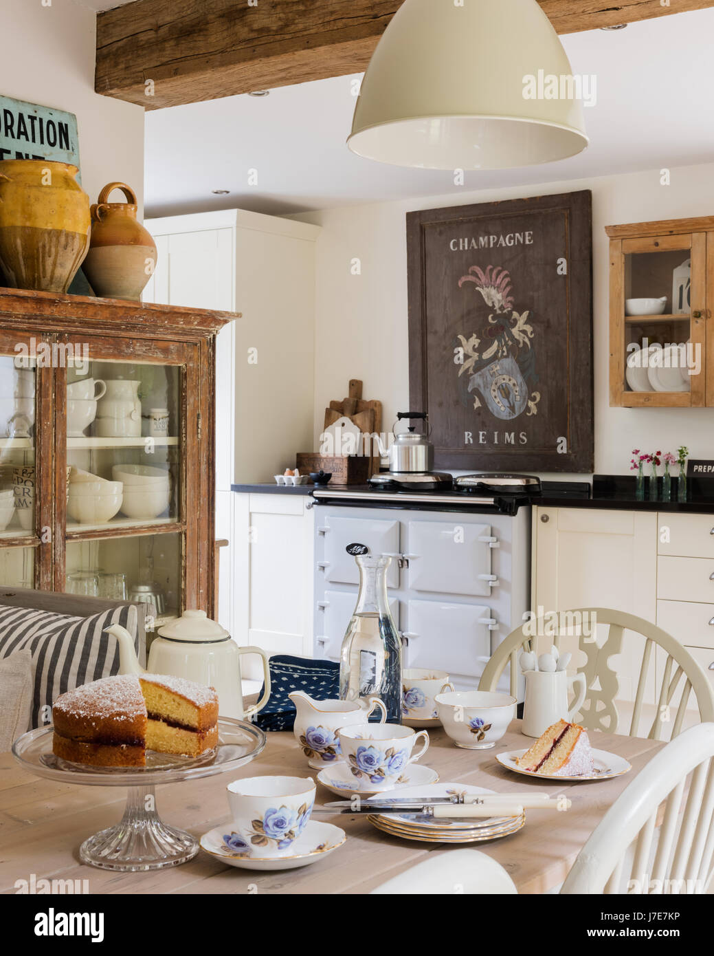 Vintage French wooden champagne sign above Aga in rustic kitchen with French feel. The table is laid for tea with Victoria sponge cake and the display Stock Photo