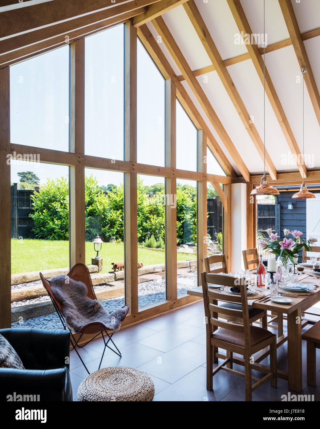 Vaulted oak-framed dining room with floor-to-ceiling windows. The table and chairs are from John Lewis and the coolicon insustrial copper pendant ligh Stock Photo