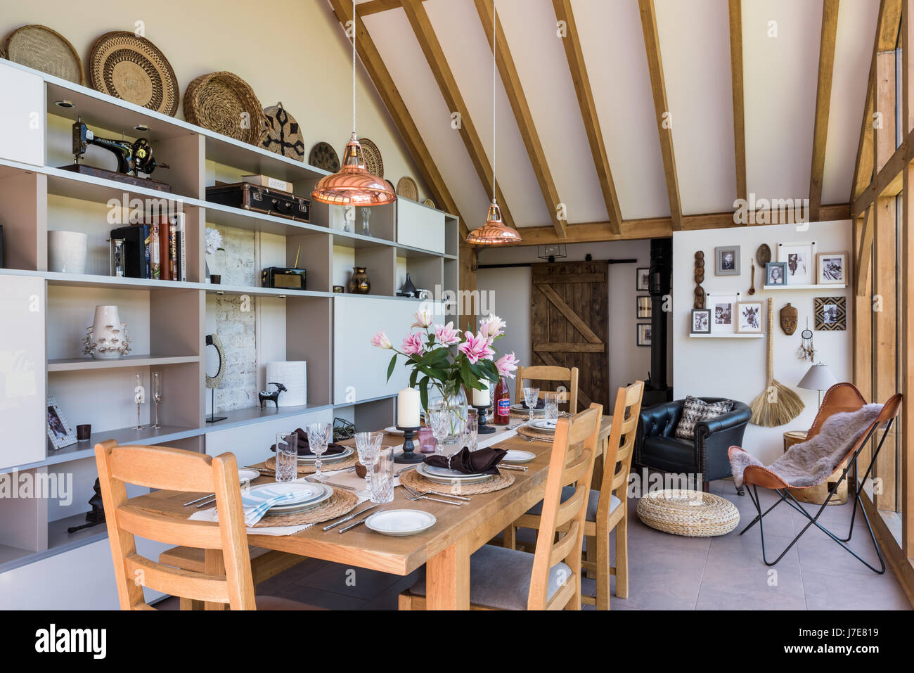 Vaulted oak-framed dining room with floor-to-ceiling windows. The table and chairs are from John Lewis and the coolicon insustrial copper pendant ligh Stock Photo