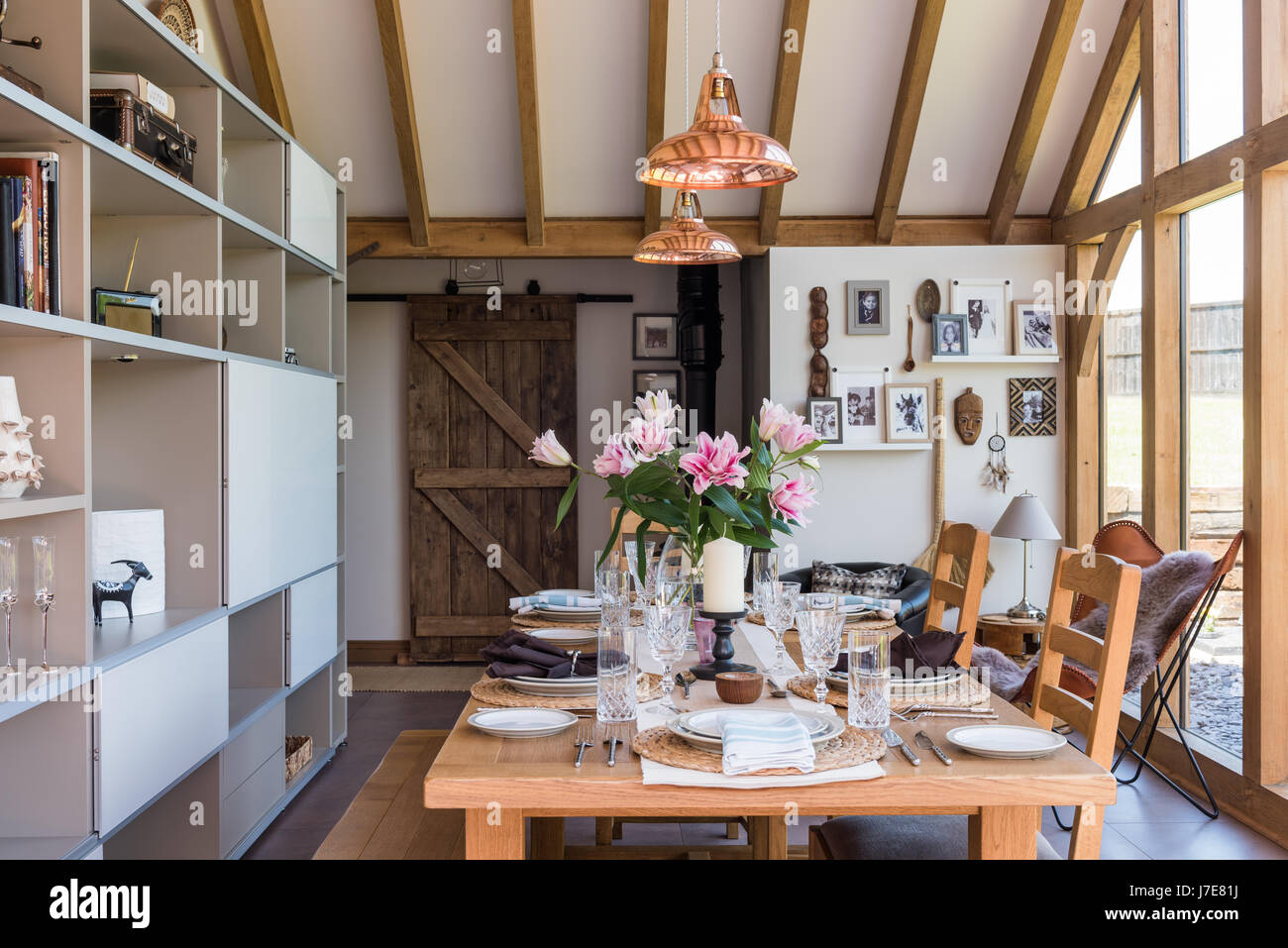 Vaulted oak-framed dining room with floor-to-ceiling windows. The table and chairs are from John Lewis and the coolicon insustrial copper pendant ligh Stock Photo