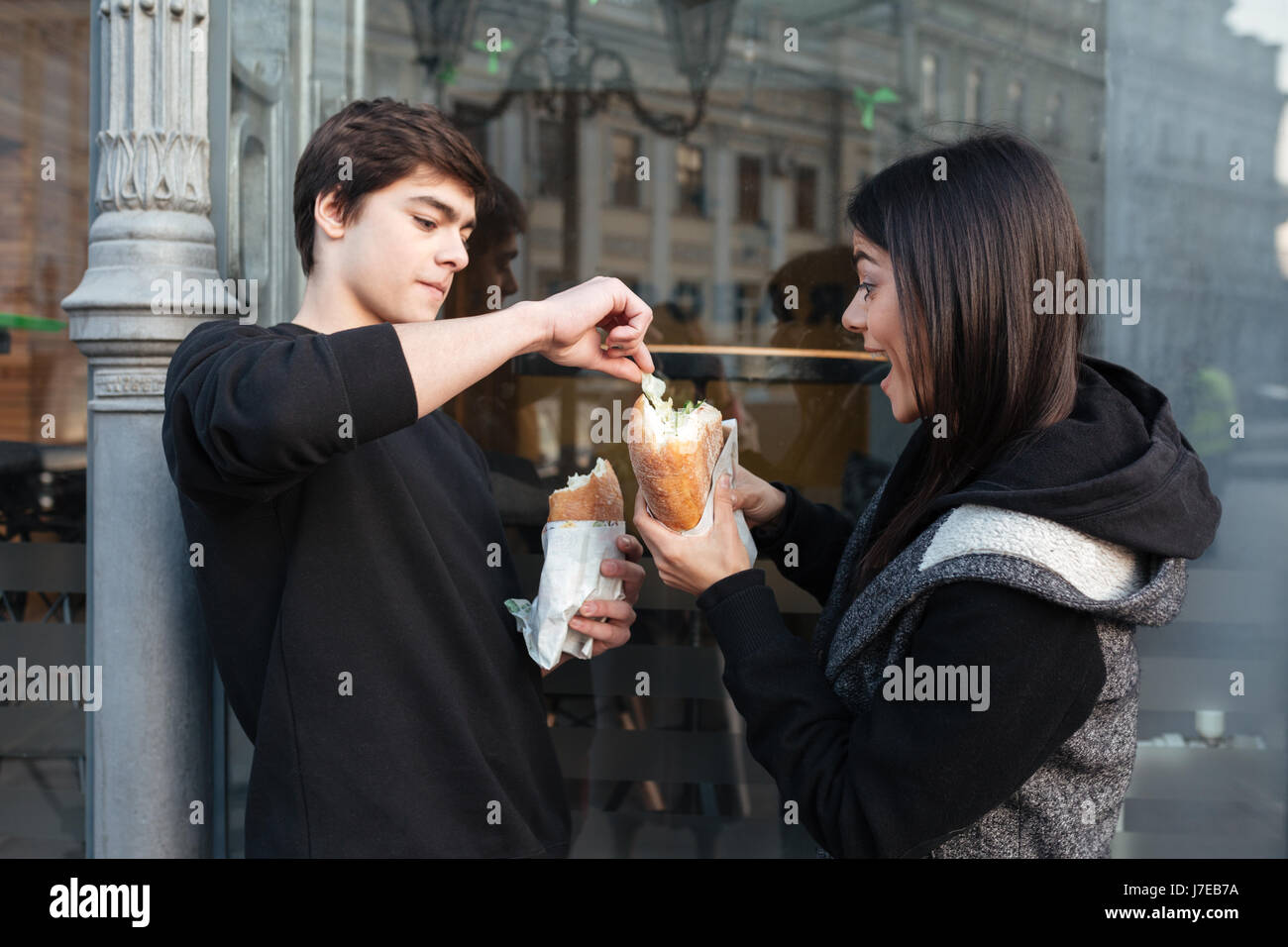Young man trying to eat burger of his sister near cafe Stock Photo