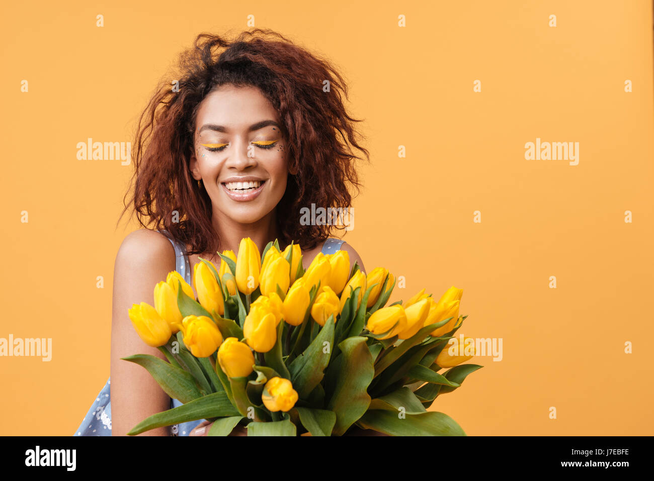 Smiling African woman with closed eyes holding bouquet of flowers over ...