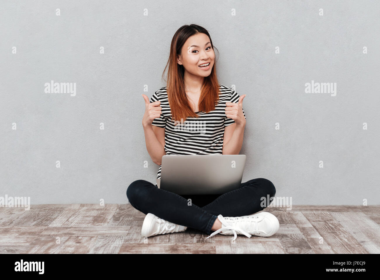 Joyful asian woman showing thumbs up while working with laptop isolated ...