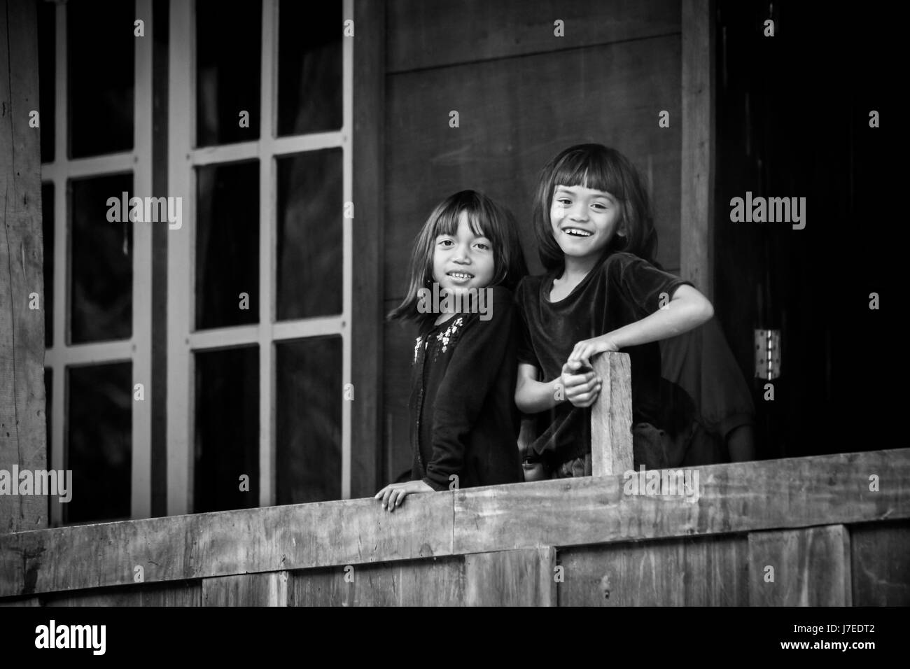 Beautiful black and white candid natural portrait image of smiling kids from the indigenous race of Torajan people in Sulawesi standing on balcony Stock Photo