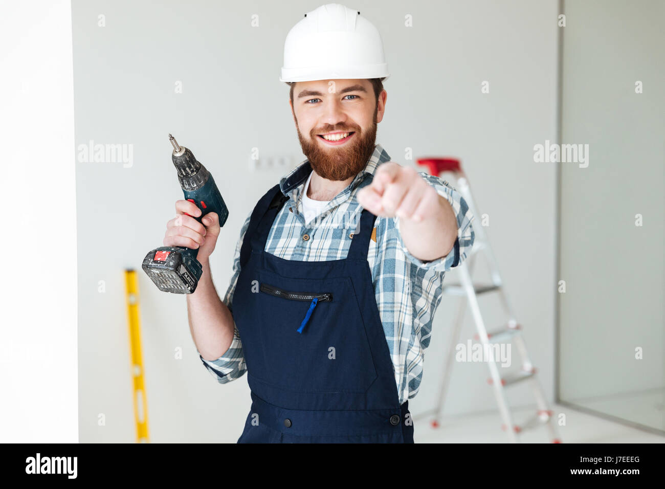 Young hardworking man with drill pointing at camera isolated Stock Photo