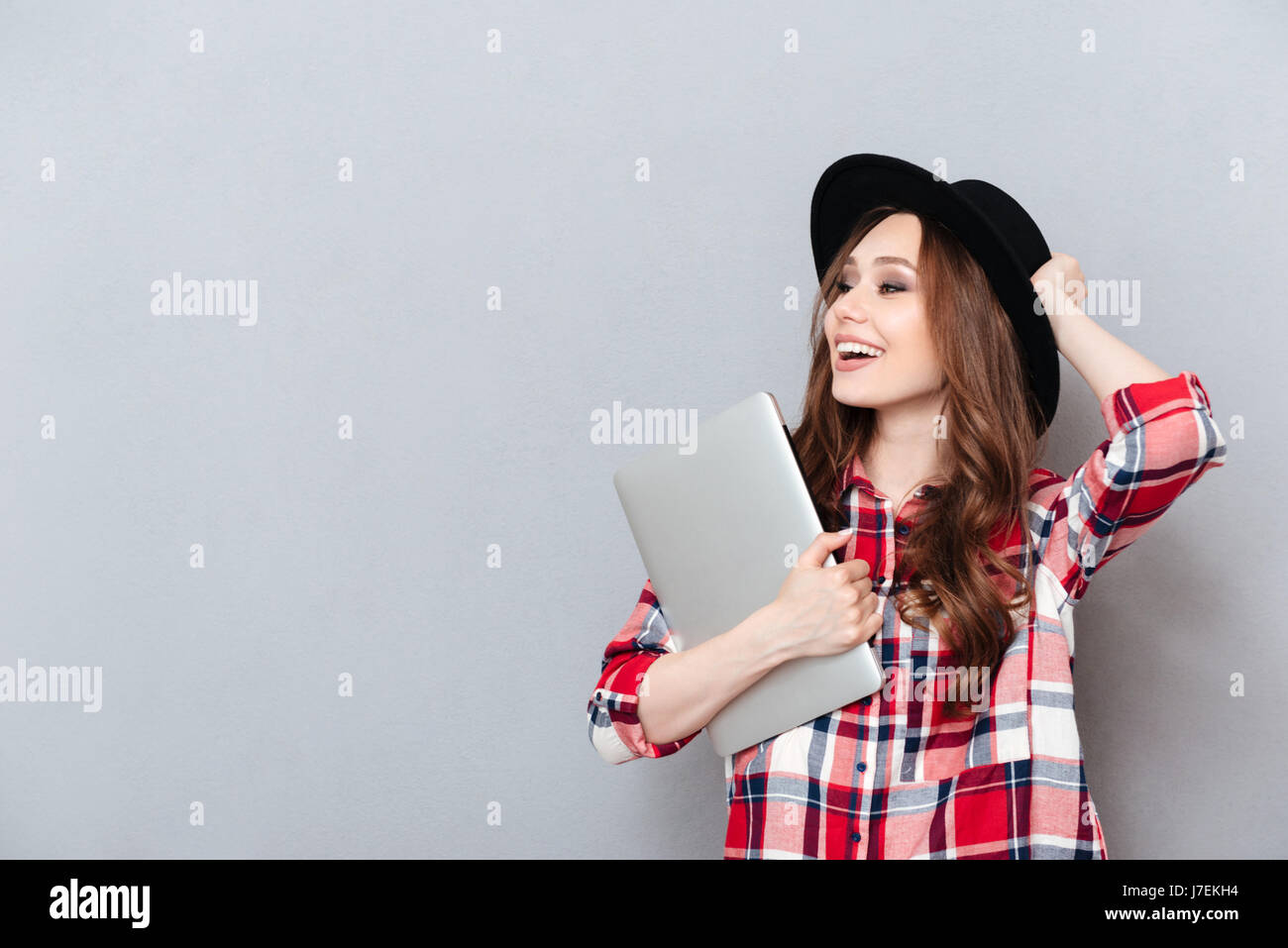 Portrait of a happy smiling teenager girl in hat holding laptop and ...