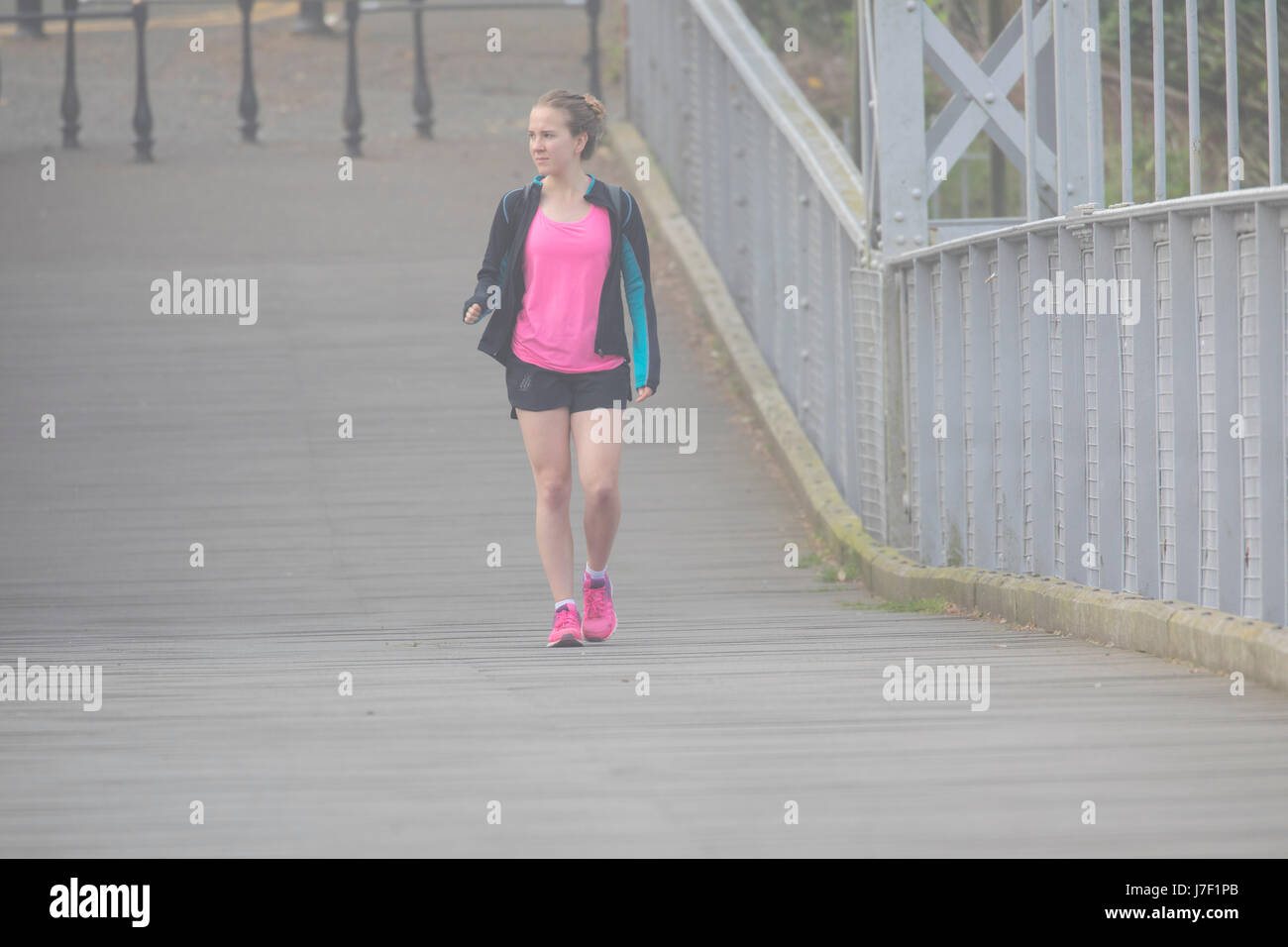 A morning jogger getting some fitness in crossing the suspension bridge over the River Dee in Chester on a very foggy, misty morning in summer Stock Photo