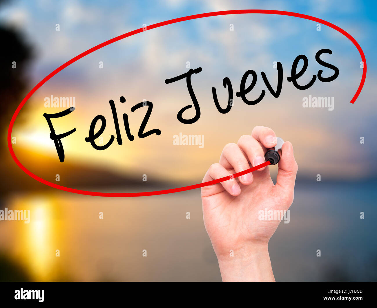 Man Hand writing Feliz Jueves (Happy Thursday In Spanish) with black