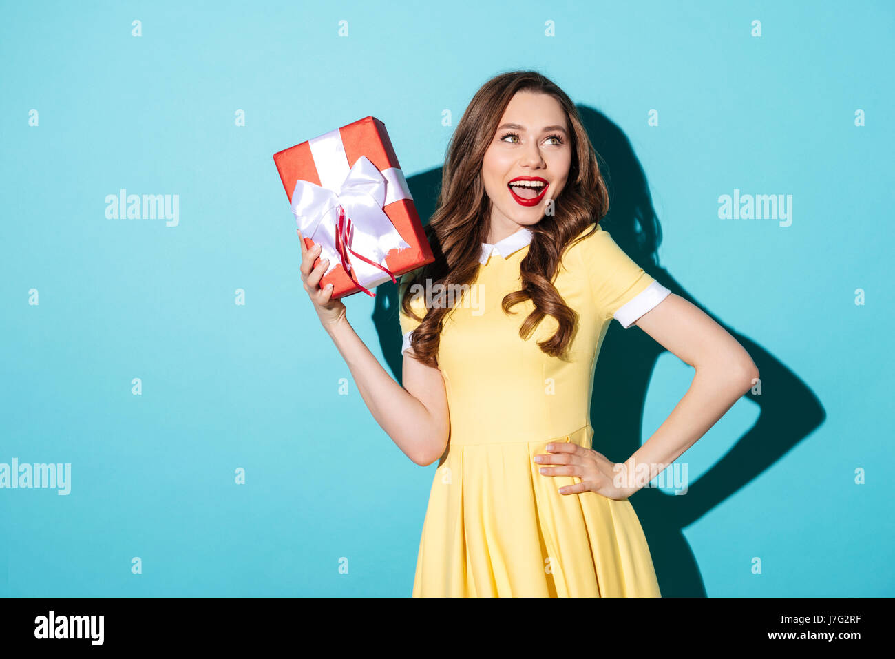 Portrait of a cute playful girl in dress holding gift box and looking ...
