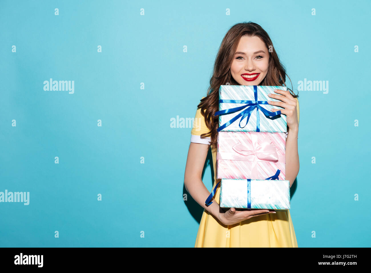 Portrait of a smiling pretty girl holding stack of gift boxes isolated ...
