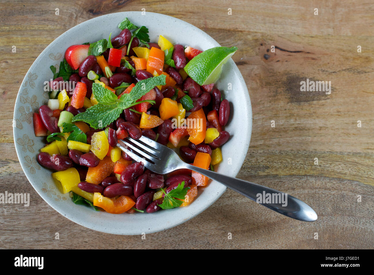 Closeup on red kidney beans and bell pepper salad served on tan plate on wooden table, decorated with mint leaves and served with a slice of lime Stock Photo