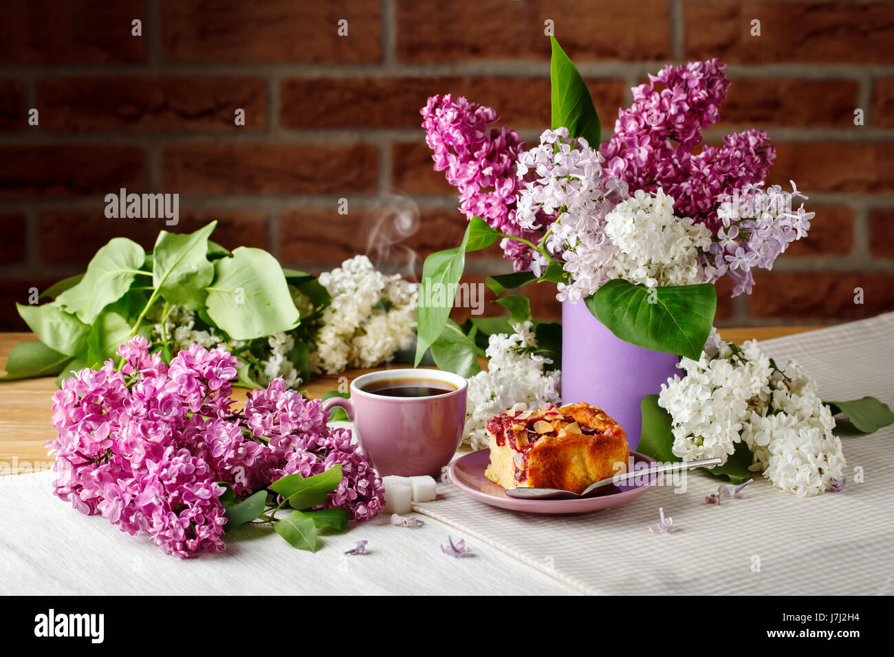 Still life with branches of lilac and a Cup of coffee on a wooden table ...