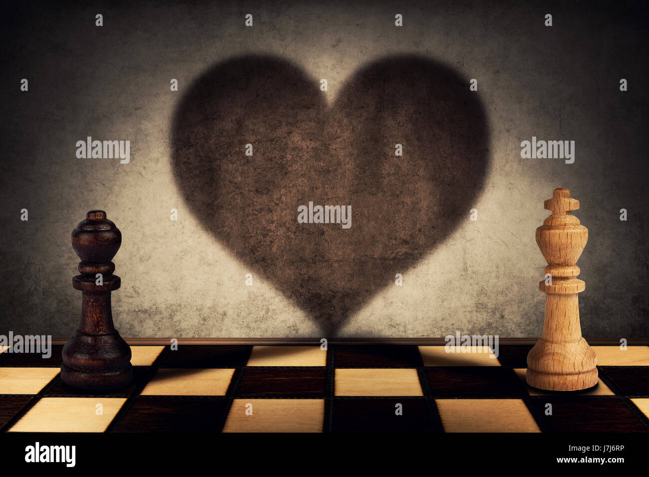 Black queen and white king chess pieces standing in front one another casting their shadows transform into a big heart on the wall. Love symbol Stock Photo