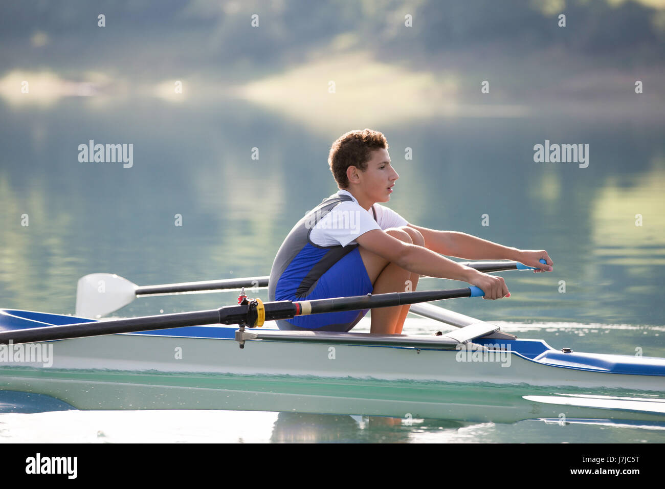 A Young single scull rowing competitor paddles on the tranquil lake ...