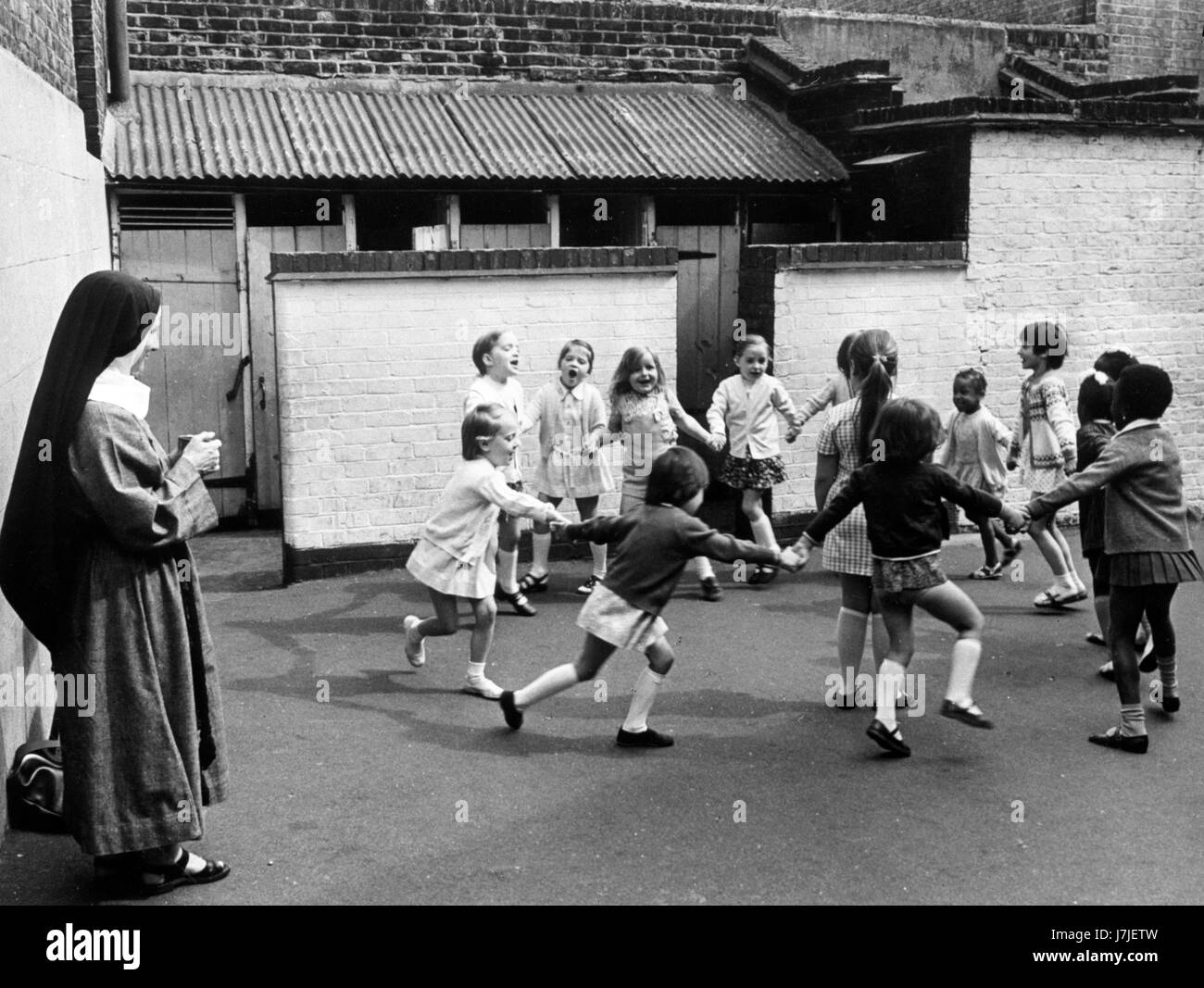 Children, supervised by a nun, play beside tumbledown exterior lavatories, which has no hot water or washing facilities, at Clerkenwell Parochial Junior Mixed and Infants' School in London. The school features in the report published by the National union of Teachers on sub-standard conditions in schools. Stock Photo