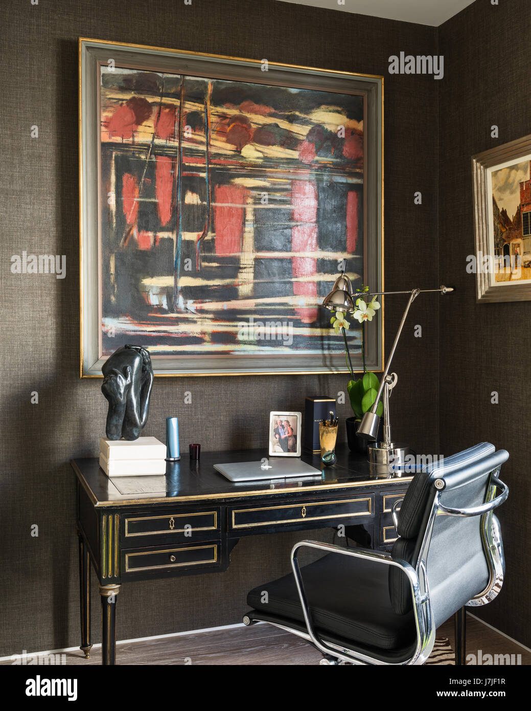 A painting by Richard Robbins above an ebonized antique desk with leather chair, the wallpaper is Her Majesty from Kandy Collection by Elitis Stock Photo