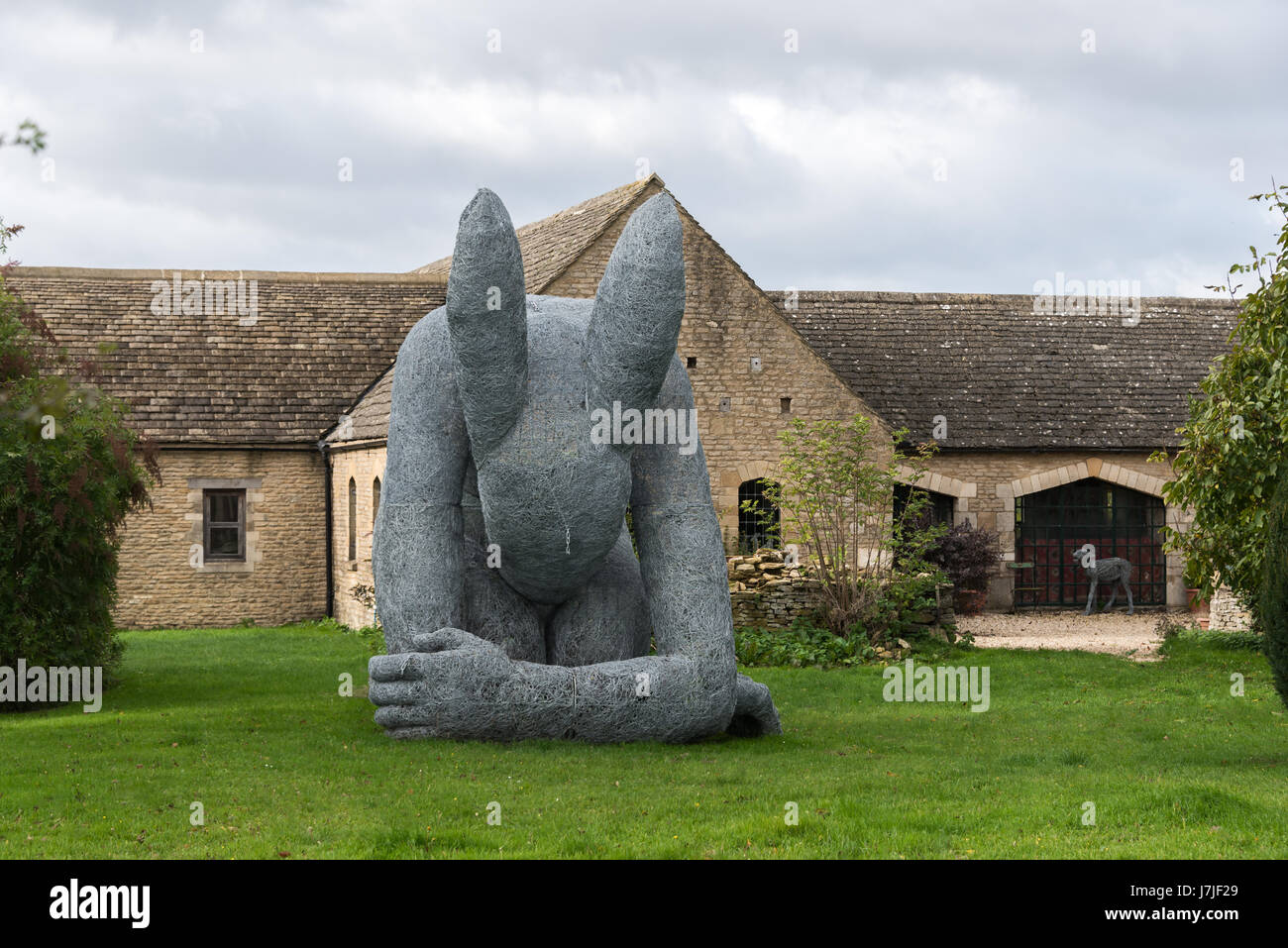 'Lady Hare' by Sophie Ryder crouched on lawn in front of converted cottage Stock Photo
