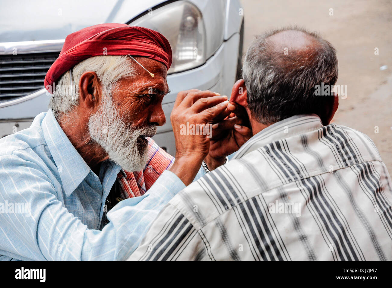 Delhi, India, september 3, 2010: Indian man cleaning man's ear on Delhi street. Stock Photo