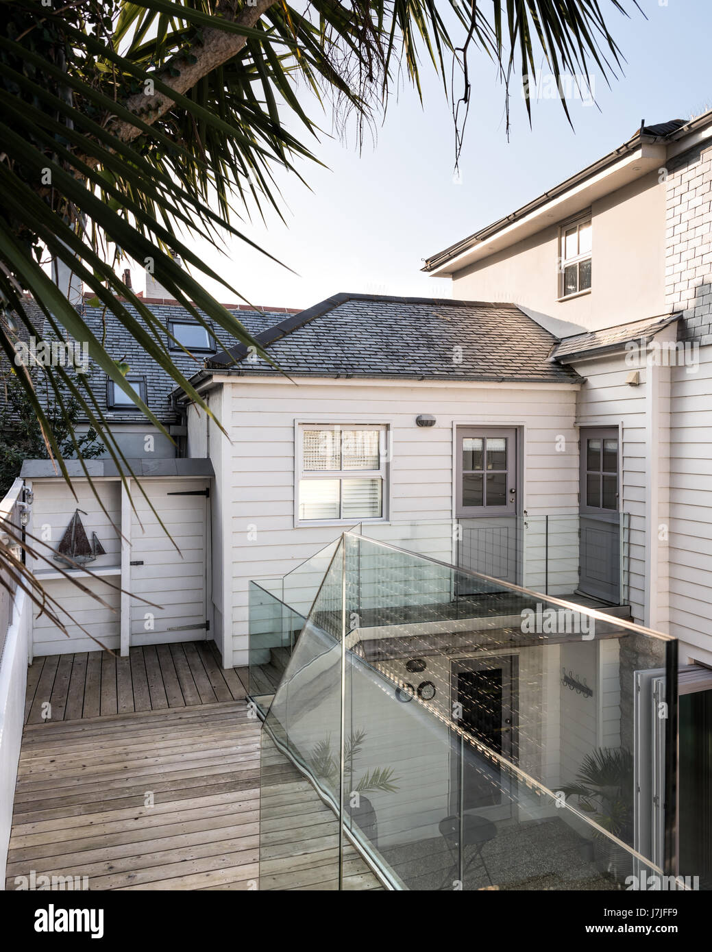 Contemporary glass balustrades and wooden decking on New England style deck of cornish holiday home. Doors painted in Lead Colour by Little Greene Stock Photo