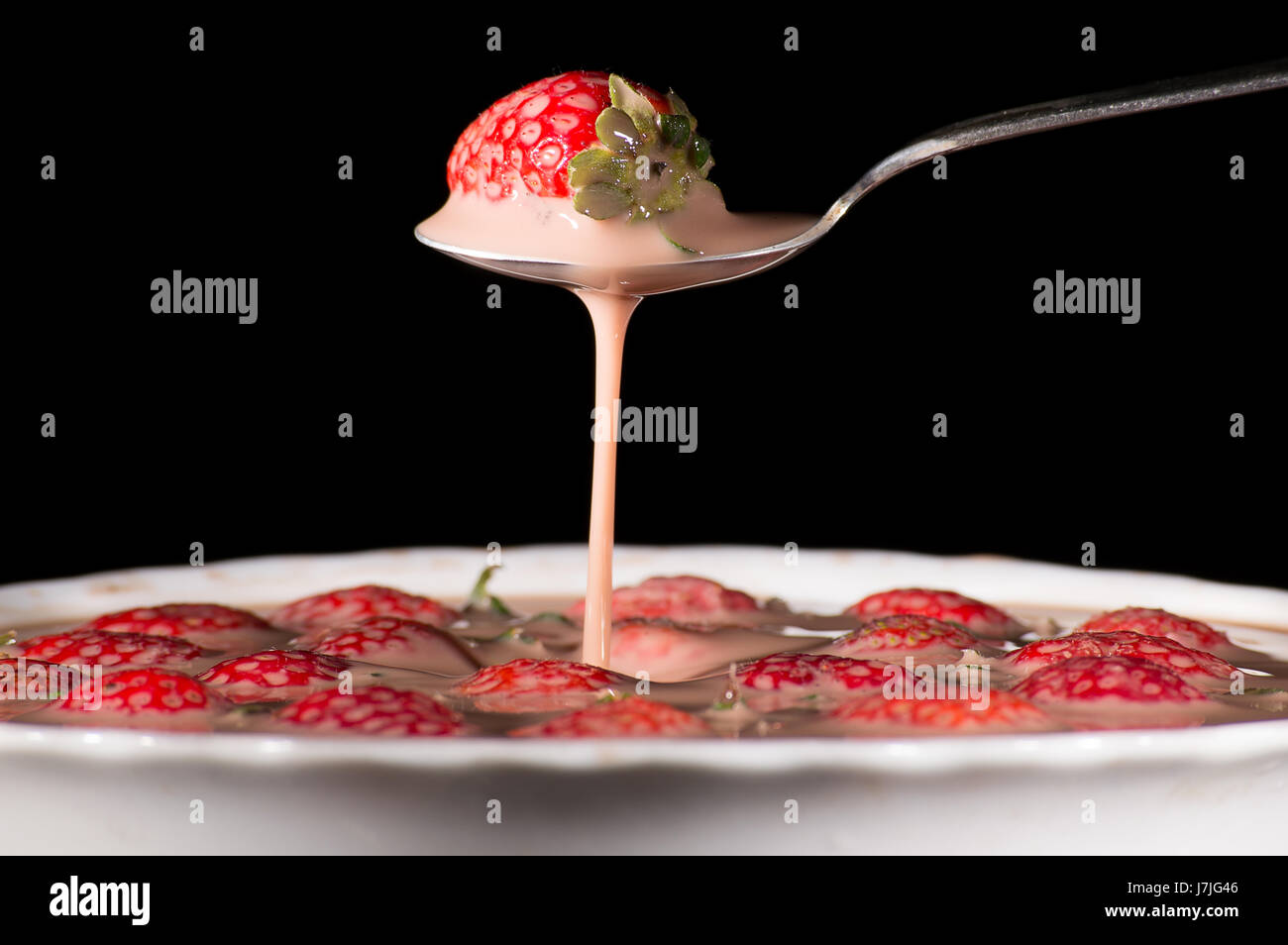 taking strawberries with spoon on black background Stock Photo