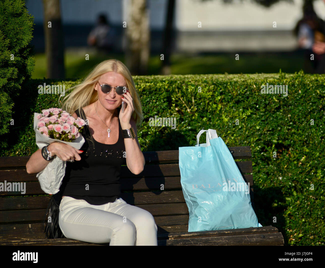 Blonde woman talking on the phone in a bench. Belgrade, Serbia Stock Photo