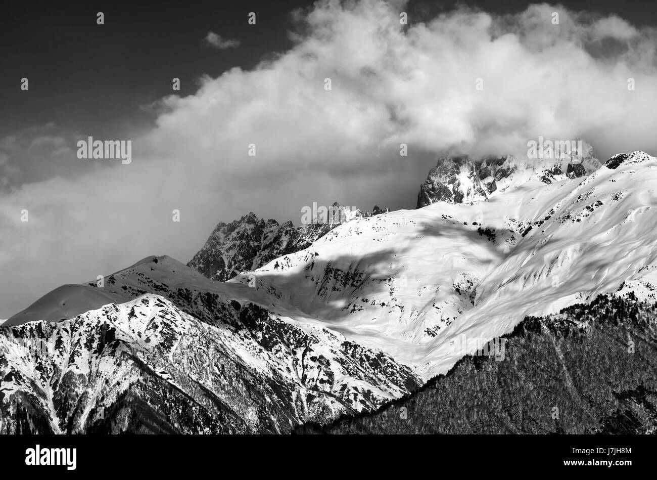 Black and white view on snow mountains in clouds in winter sun day. Mounts Ushba, Caucasus Mountains. Svaneti region of Georgia. Stock Photo
