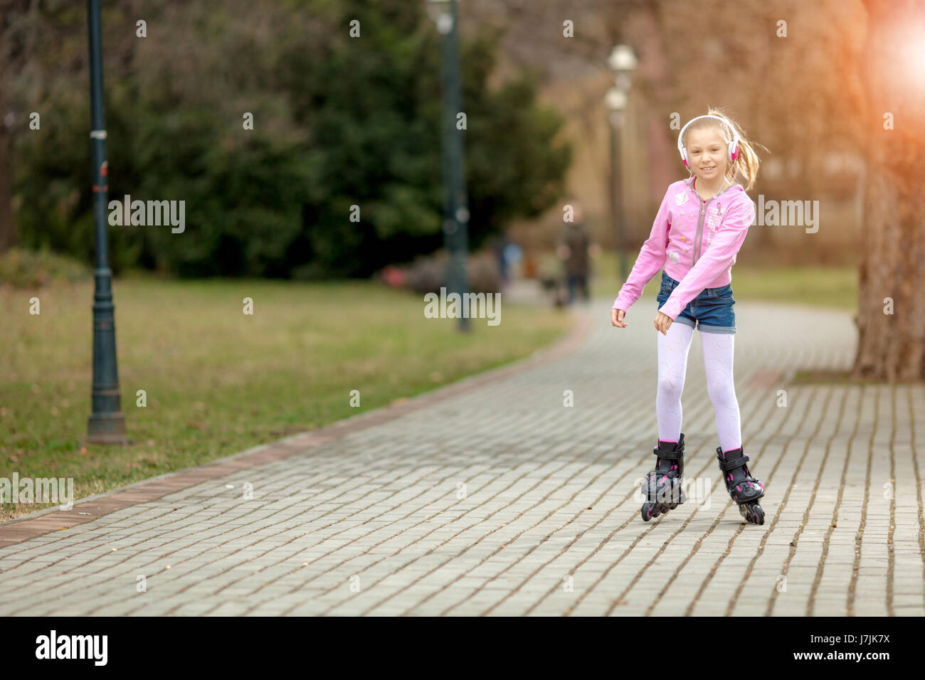 Beautiful smiling little girl inline skating through the park Stock