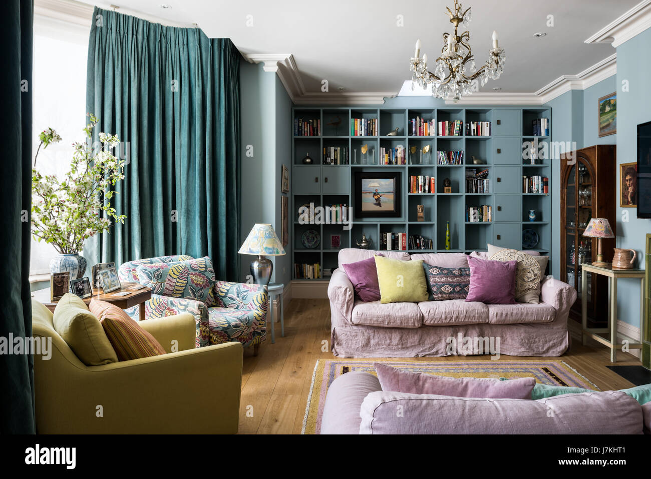 Colourful sitting room with dusty pink upholstered sofas and assorted cushion fabrics. The floor-length curtains are a shade of teal Stock Photo
