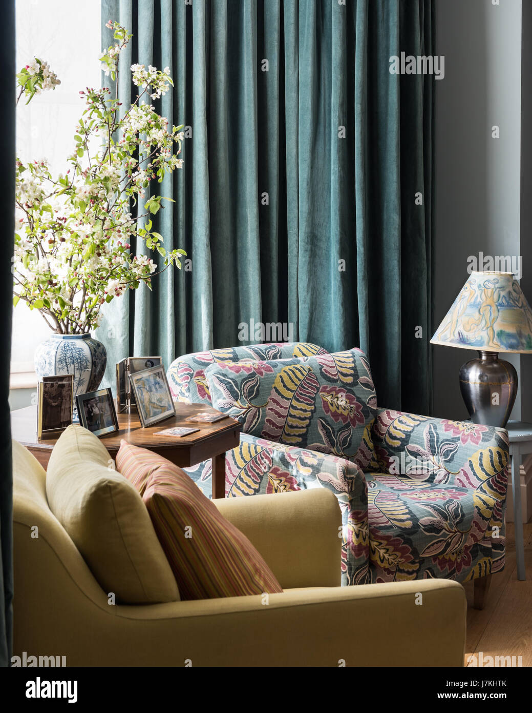 Leaf patterned upholstered armchair in sitting room with floor length teal curtains Stock Photo
